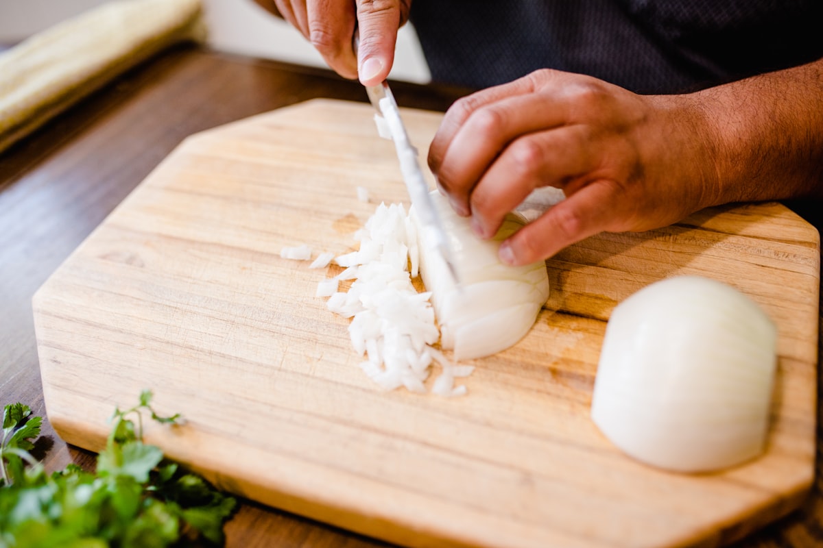 Person dicing a white onion on a wooden cutting board