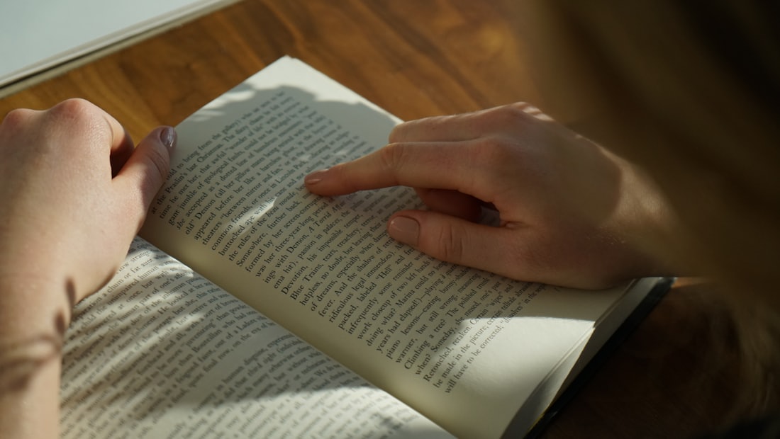 Person reading a book at a wooden table