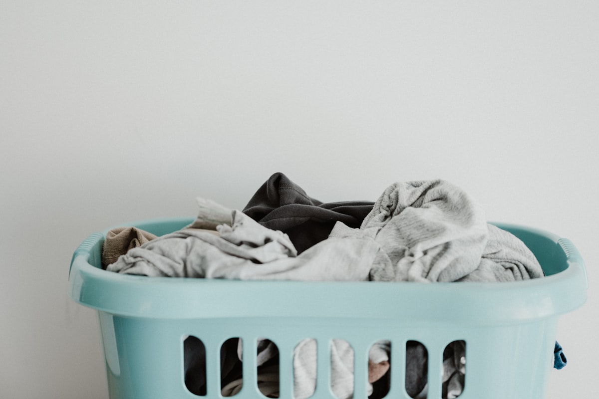 Laundry basket full of clothes against a plain wall